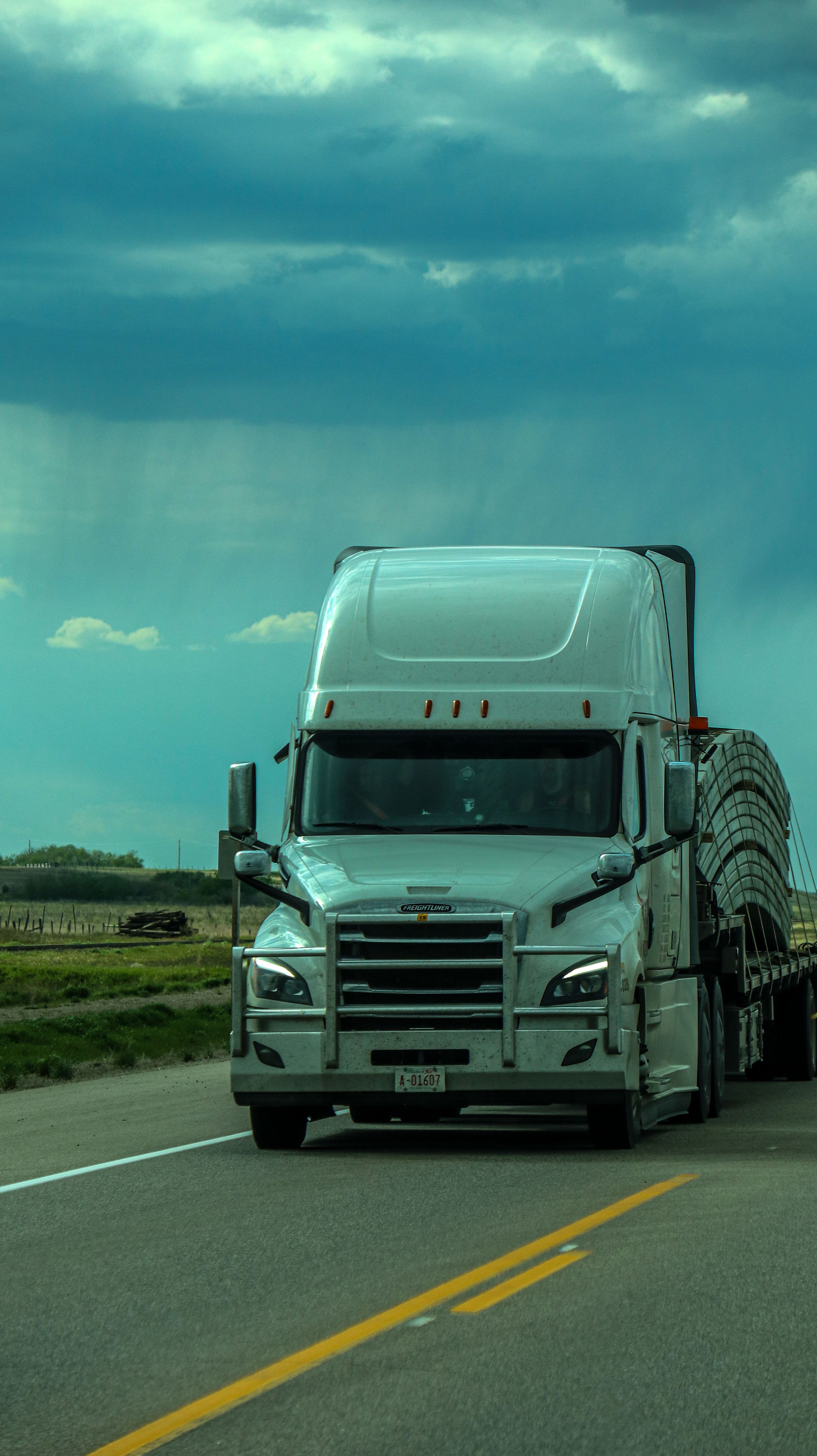 A semi-truck driving toward the camera on a two-lane highway under a dramatic stormy sky