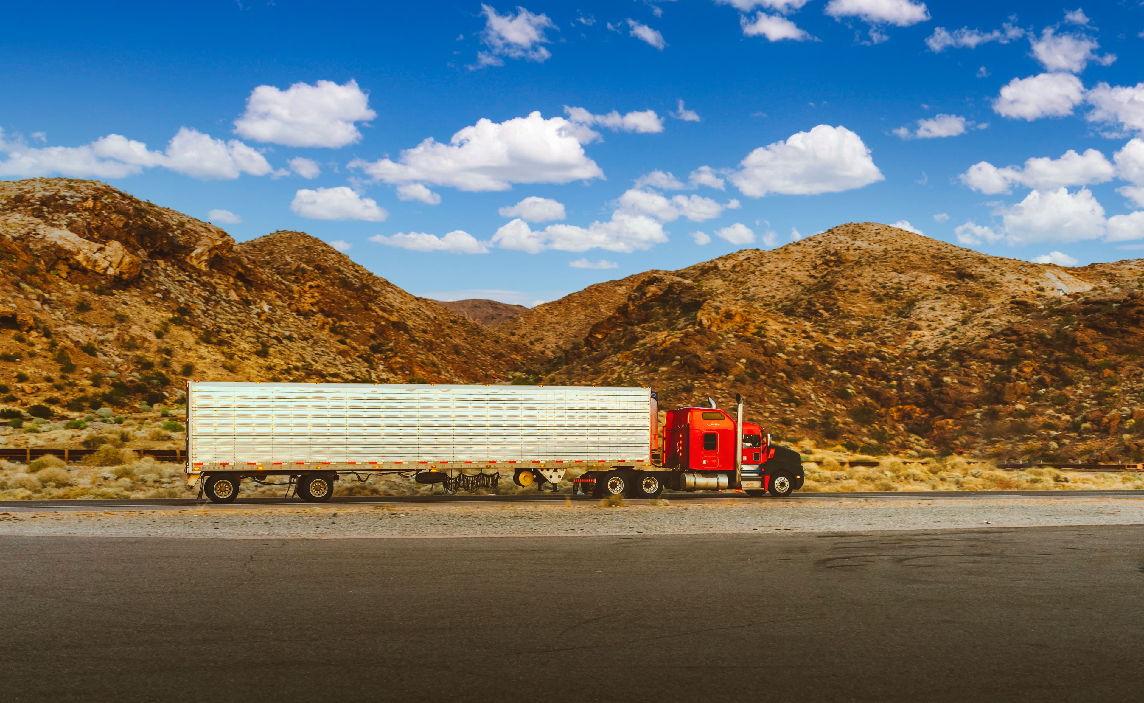 A semi-truck driving a desert highway under a clear blue sky